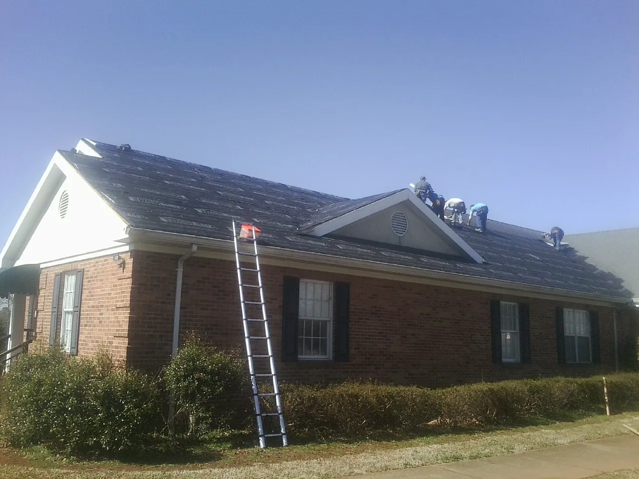 Crew tearing shingles off a brick ranch roof with a ladder set — Metal Roof Repair work by our crew in Bowling Green